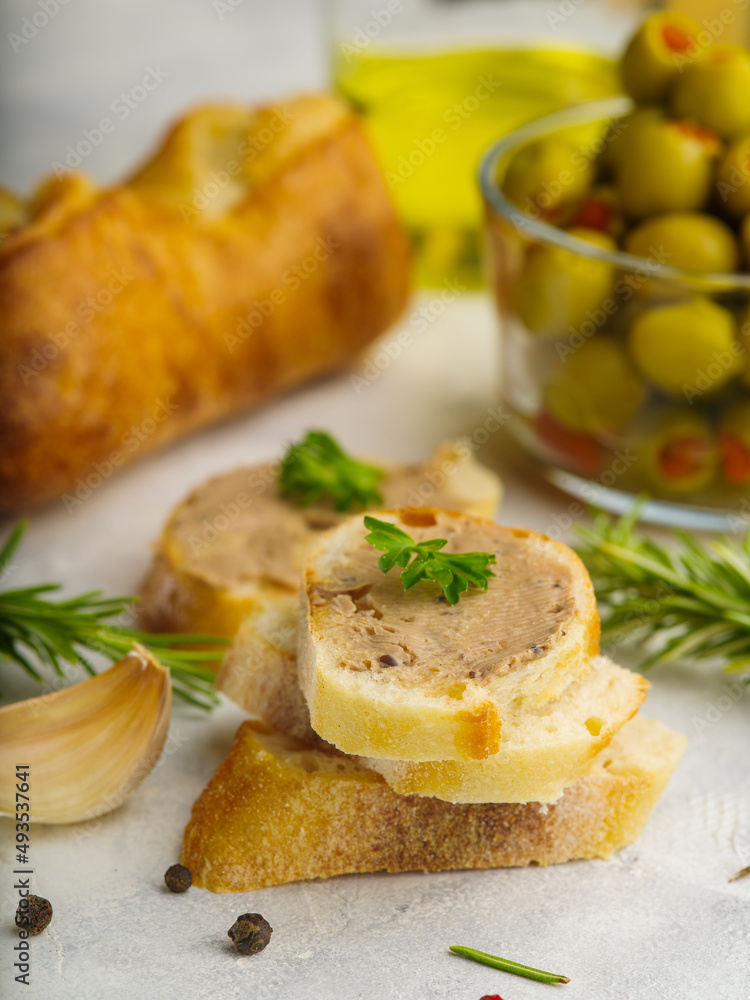 Close-up. French foie gras baguette sandwiches garnished with parsley leaves, green olives, baguette and rosemary sprigs on a white background. Festive dish. French cuisine...