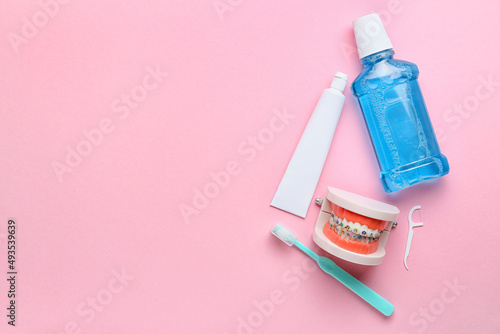 Model of jaw with dental braces, tooth brush, paste and rinse on pink background