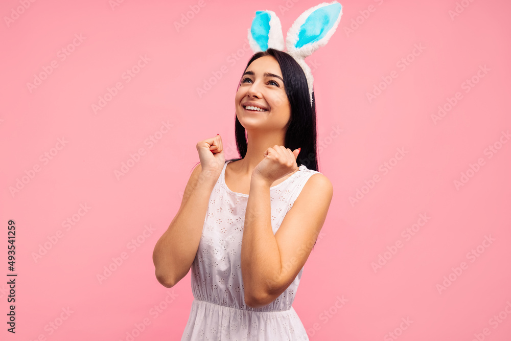 Cheerful emotional woman in rabbit ears, in a white dress on a pink background. Easter. Christ's Resurrection
