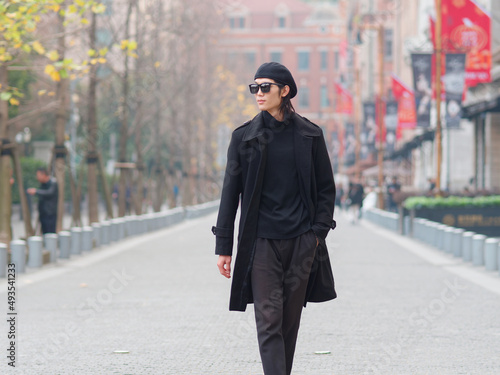 Portrait of handsome Chinese young man wearing black overcoat, sweater and trousers with sunglasses walking on Shanghai street, front view, male fashion, cool Asian young man lifestyle. © atiger