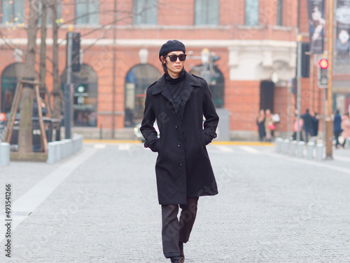 Photography Portrait of handsome Chinese young man wearing black overcoat, sweater and trousers with sunglasses walking on Shanghai street, front view, male fashion, cool Asian young man lifestyle
