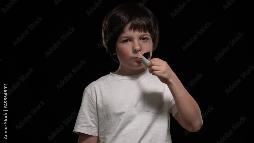 Front view of Caucasian sad boy looking at camera unsticking adhesive tape from mouth. Portrait of abused child posing at black background with upset facial expression. Abuse and bullying concept Front view of Caucasian sad boy looking at camera unsticking adhesive tape from mouth. Portrait of abused child posing at black background with upset facial expression. Abuse and bullying concept