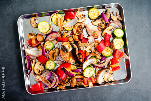 Overhead View of Raw Vegetables Seasoned with Olive Oil and Spices: Sliced and seasoned mushrooms, zucchini, bell peppers, onions, vegetables on a sheet pan 