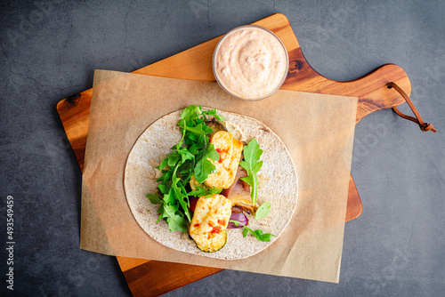 Assembling a Roasted Vegetable and Halloumi Wrap: A whole wheat flatbread topped with roasted vegetables, hummus, halloumi cheese, and harissa sauce photo