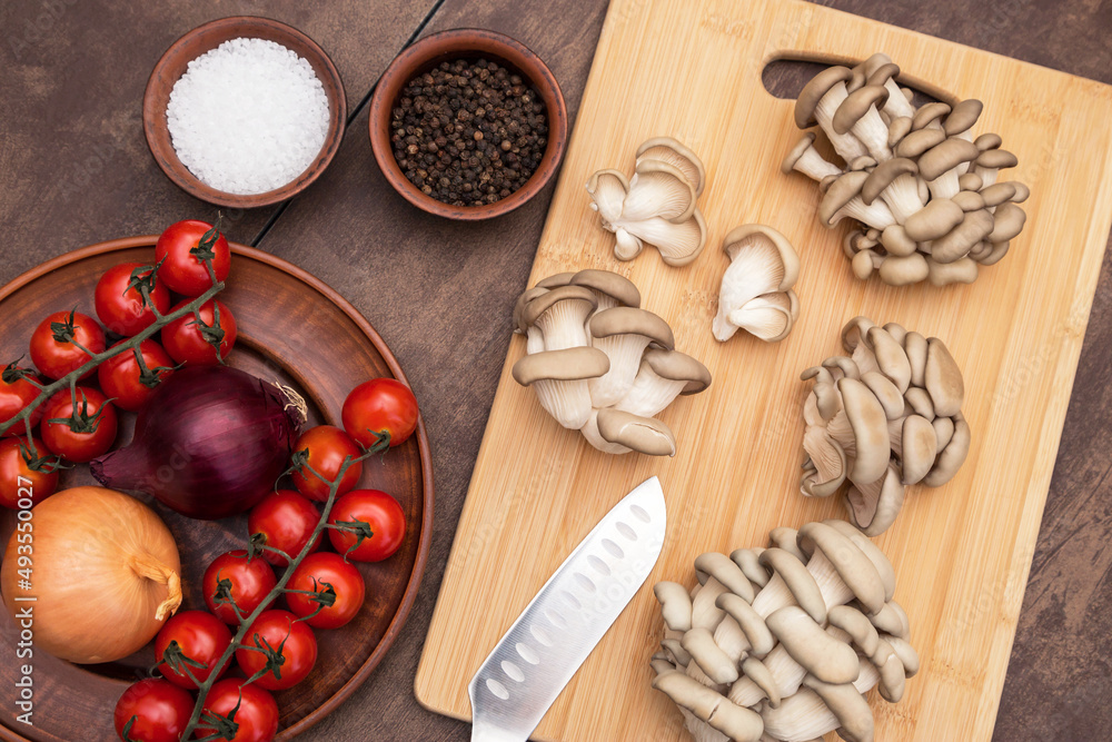 Oyster mushroom on wooden cutting board on kitchen top view, flat lay. Cooking vegan vegetarian diet dish with tomato, onion and mushrooms