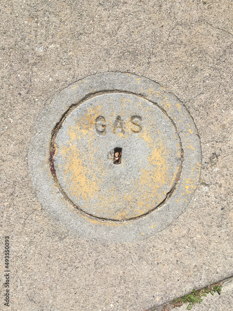 Close-up view of a small concrete cover plate for a gas valve on a city street sidewalk