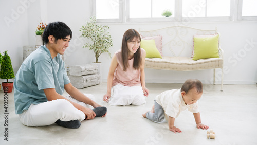 部屋で遊ぶ赤ちゃんとそれを見守る両親