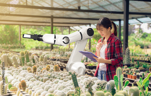 Robotic arm agriculture smart farm automation futuristic technology working with female farmer engineer, mechanical hand planting plants and trees in greenhouse, efficient working  machinery function. photo