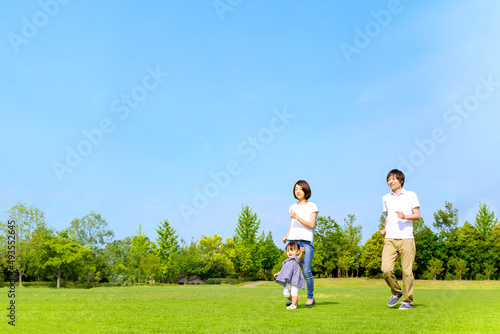 青空を背景に緑の芝の上で一緒に走る幸せな娘と若いカップル。家族,幸せ,愛情,育児のイメージ