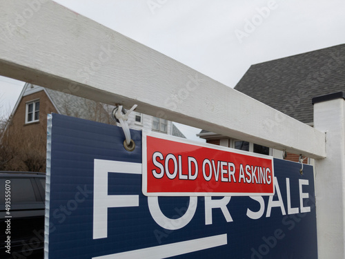 Sign sold over asking price  in front of a detached house in residential area. Real estate bubble, hot housing market, overpriced property, buyer activity, spring and summer sale concept. photo