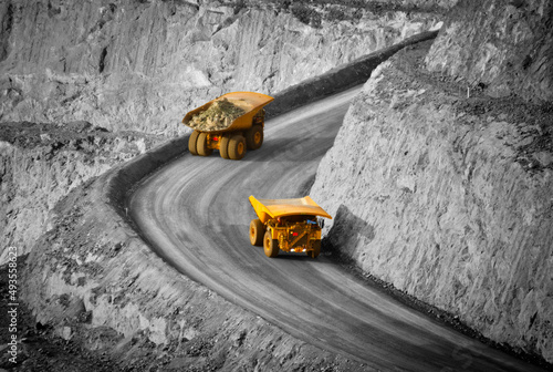 Two trucks in a modern gold mine in Australia. Spot colour large haul trucks transport gold ore from the pit, Opencast mine. Yellow trucks, black and white background. - All logos removed.