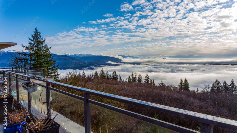Fototapeta premium Dense cloud inversion over valley with alpine mountain backdrop as seen from a BC patio.