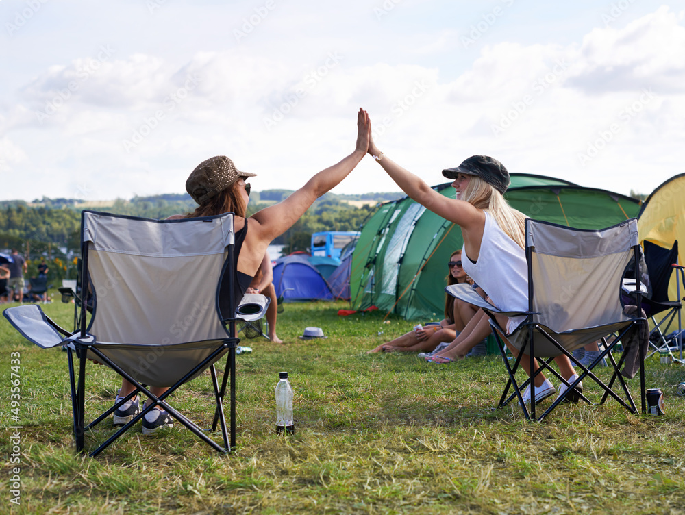 Happy campers. Rearview shot of two friends giving each other a high five at an outdoor festival. - obrazy, fototapety, plakaty 