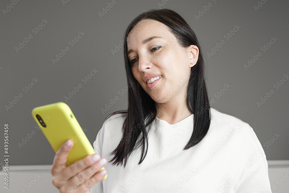 A brunette blogger girl in a white T-shirt with a bright yellow phone is browsing social networks through her smartphone or communicating with subscribers. A brunette blogger girl in a white T-shirt with a bright yellow phone is browsing social networks through her smartphone or communicating with subscribers.