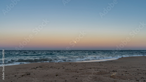 A quiet evening on the Red Sea beach. The full moon shines in a bluish-pink sky. Turquoise waves roll on the sand and foam. Egypt