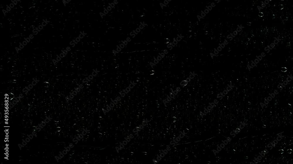 Closeup water rainfall, rain drops falling on window glass over black background Closeup water rainfall, rain drops falling on window glass over black background