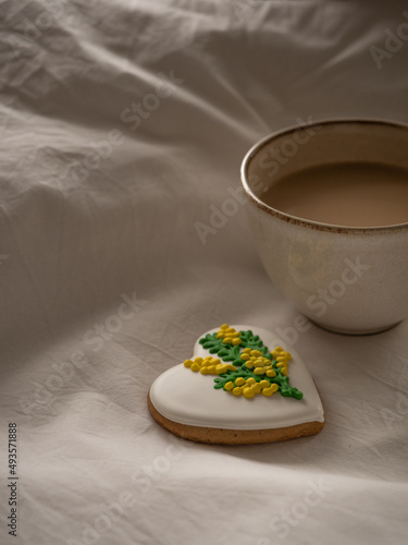 Morning coffee with milk with heart-shaped cookies painted with mimosa pattern icing  on a white bed in the morning light