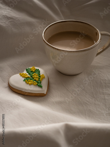 Morning coffee with milk with heart-shaped cookies painted with mimosa pattern icing  on a white bed in the morning light