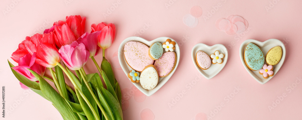 Happy Easter. Multi-colored pastel easter cookies gingerbread, seasonal flowers tulips on pink background. Easter concept, copy space, flyer, banner, coupon, greeting card, invitation Happy Easter. Multi-colored pastel easter cookies gingerbread, seasonal flowers tulips on pink background. Easter concept, copy space, flyer, banner, coupon, greeting card, invitation