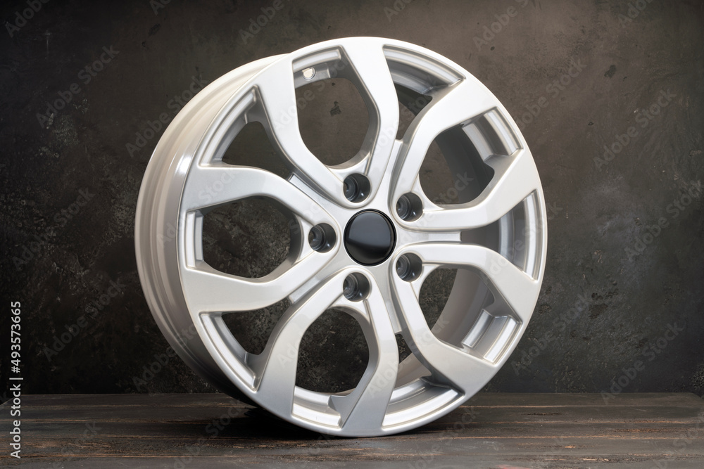 new grey alloy wheels on a dark textured black background. a wheel for a car