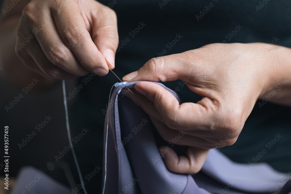 Woman hands putting needle with thread to the cloth button as sewing for repairing.