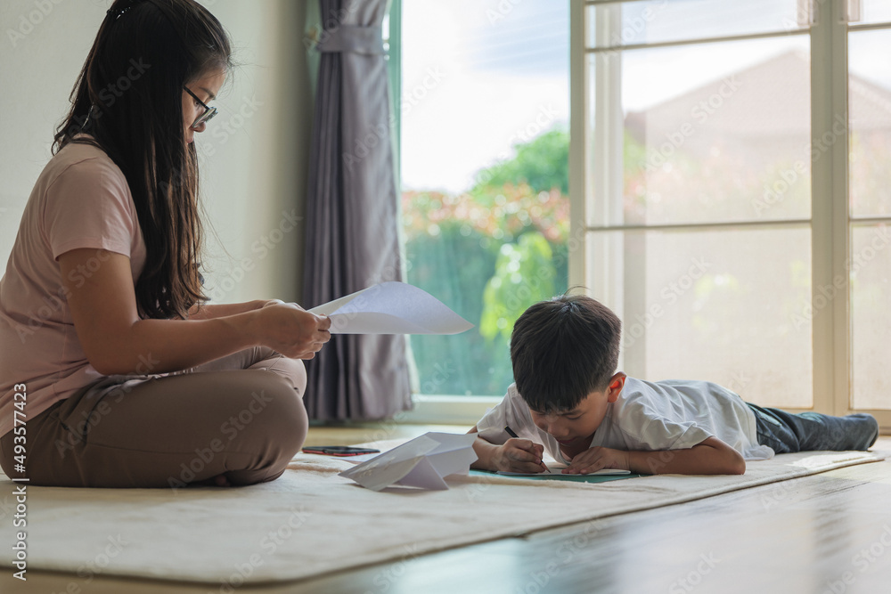 Asian boy about 5 years olds in folding a paper airplane with his mother as a casual playing at home. Asian boy about 5 years olds in folding a paper airplane with his mother as a casual playing at home.
