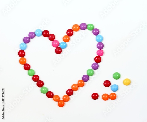 Sweet heart made from colored smarties. Chocolate candies in a shape of heart on white background, flat lay.