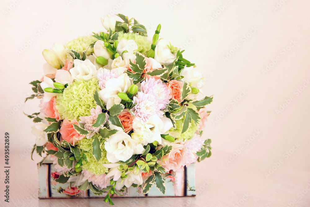 Round mint and peach colors bouquet and book on pink background. It consists of white freesia, green dianthus, peach roses, light chrysanthemum and fresh greens. Bouquet for the bride or woman.
