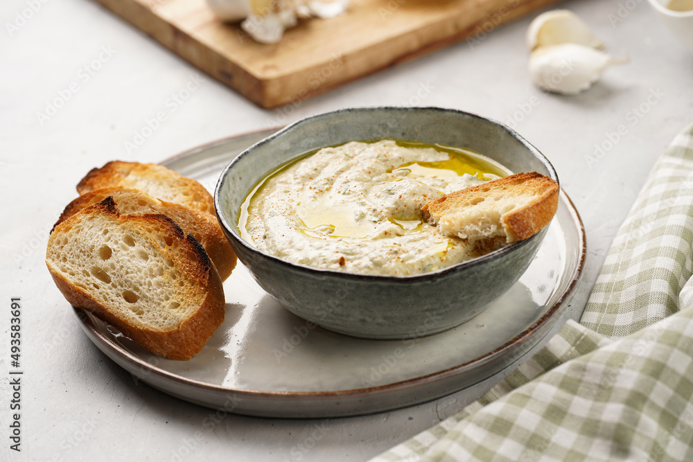 Traditional dish of arabic cuisine baba ganoush made of roasted eggplant, tahin, cilantro, garlic, olive oil, lemon juice with toasted baguette croutons on grey background Traditional dish of arabic cuisine baba ganoush made of roasted eggplant, tahin, cilantro, garlic, olive oil, lemon juice with toasted baguette croutons on grey background