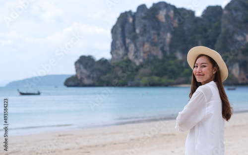 Portrait image of a beautiful young asian woman close her eyes while strolling on the beach with the sea and blue sky background