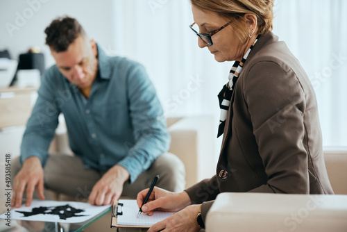 Fotografie Mature psychiatrist takes notes while her patient is doing inkblot test during their meeting