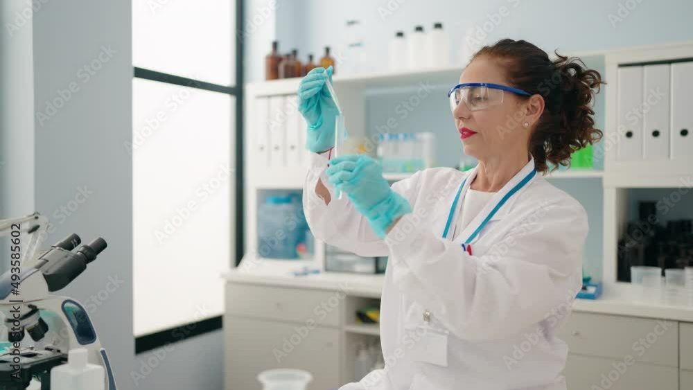 Middle age woman wearing scientist uniform pouring liquid on test tube at laboratory Middle age woman wearing scientist uniform pouring liquid on test tube at laboratory
