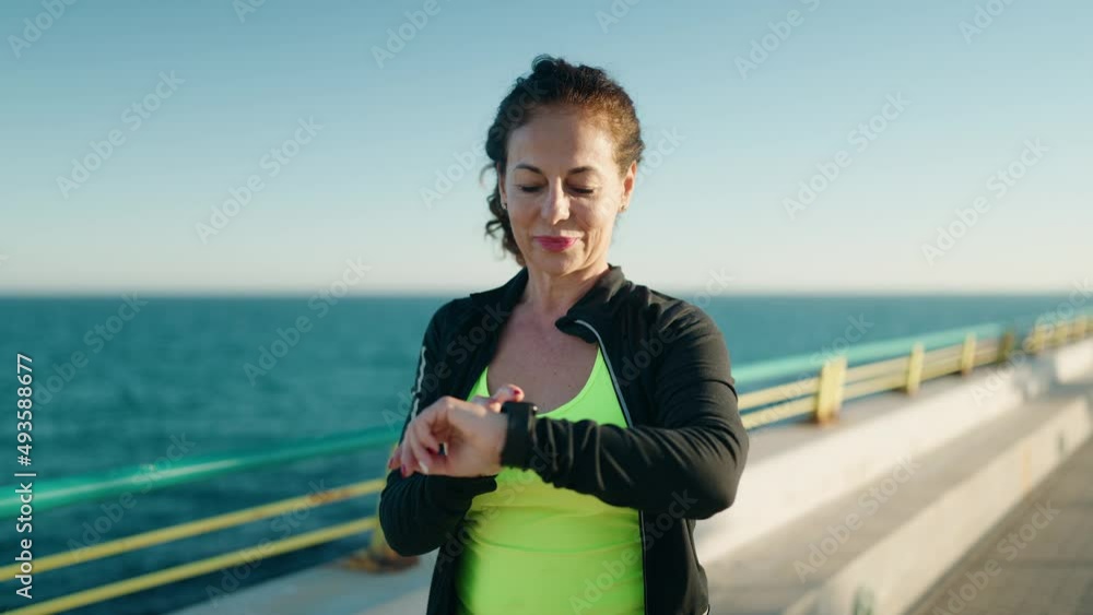 Middle age woman wearing sportswear smiling confident looking stopwatch at seaside Middle age woman wearing sportswear smiling confident looking stopwatch at seaside