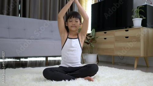 Little Asian girl sitting on carpet closed her eye and place two hands on chest in meditation asana pose at home photo