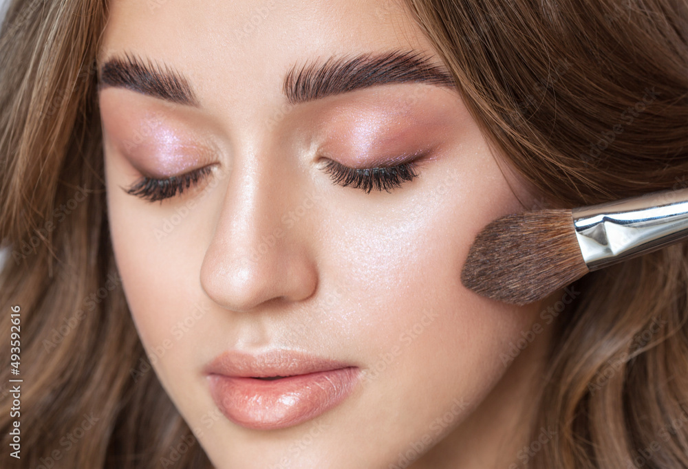 Portrait of a beautiful brunette girl with beautiful fresh makeup and healthy clean skin.Makeup artist holds a powder brush in her hands. Professional makeup concept Portrait of a beautiful brunette girl with beautiful fresh makeup and healthy clean skin.Makeup artist holds a powder brush in her hands. Professional makeup concept