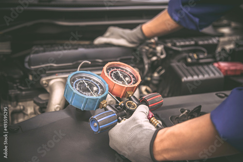 Close up hand of auto mechanic using measuring manifold gauge check the refrigerant and filling car air conditioner for fix and checking for repair service support maintenance and car insurance.