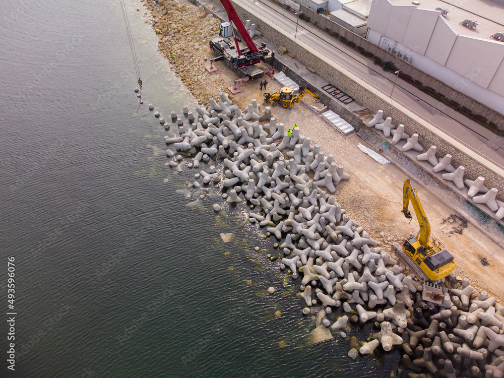 Aerial view of breakwater construction. Bulldozer and crane on a pile of boulders in the sea - obrazy, fototapety, plakaty 