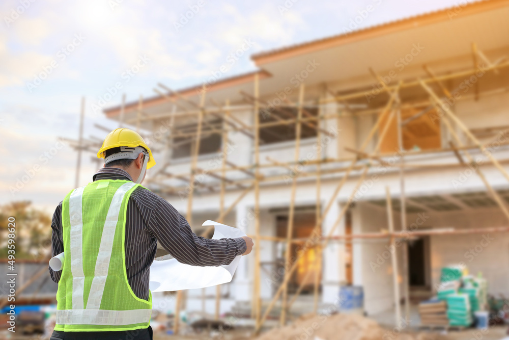 young professional engineer in protective helmet and blueprints paper at the house building construction site young professional engineer in protective helmet and blueprints paper at the house building construction site
