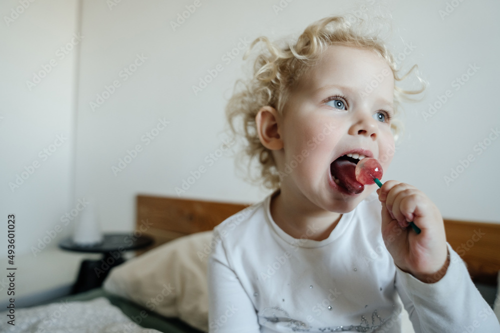 little child blonde curly eats sweet candy on a stick. Health and care for children's dental health. little child blonde curly eats sweet candy on a stick. Health and care for children's dental health.
