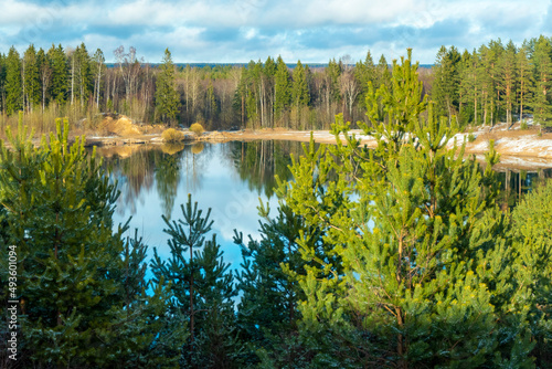 Spring landscape with a beautiful lake with fir trees and last snow against a cloudy sky