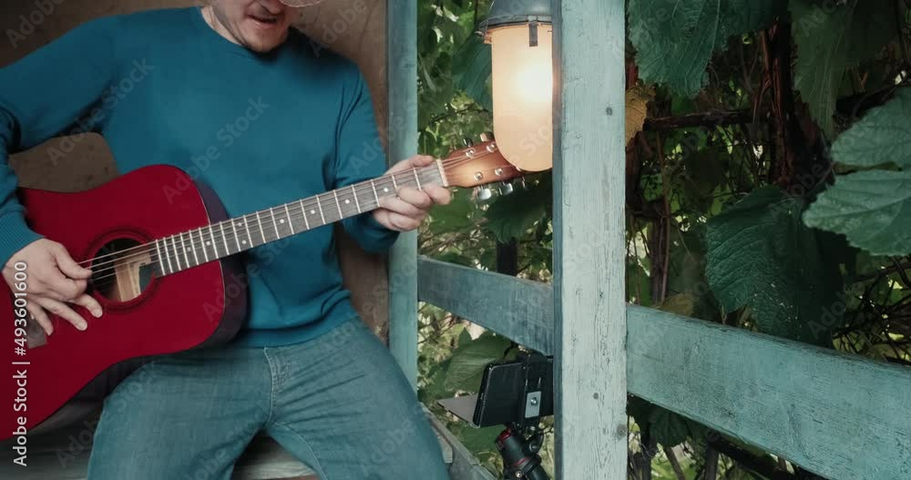 Man in a cowboy hat with an acoustic guitar on the porch of an old house portrays a rock musician. The concept of humor and parody of rock, metal bands Man in a cowboy hat with an acoustic guitar on the porch of an old house portrays a rock musician. The concept of humor and parody of rock, metal bands