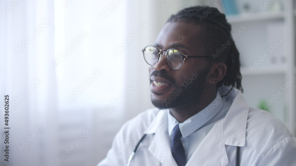 Confident African American general practitioner in eyeglasses listening to patient's complains, concluding diagnosis
