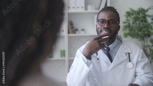 Handsome African American doctor carefully listening to his female patient, health check-up