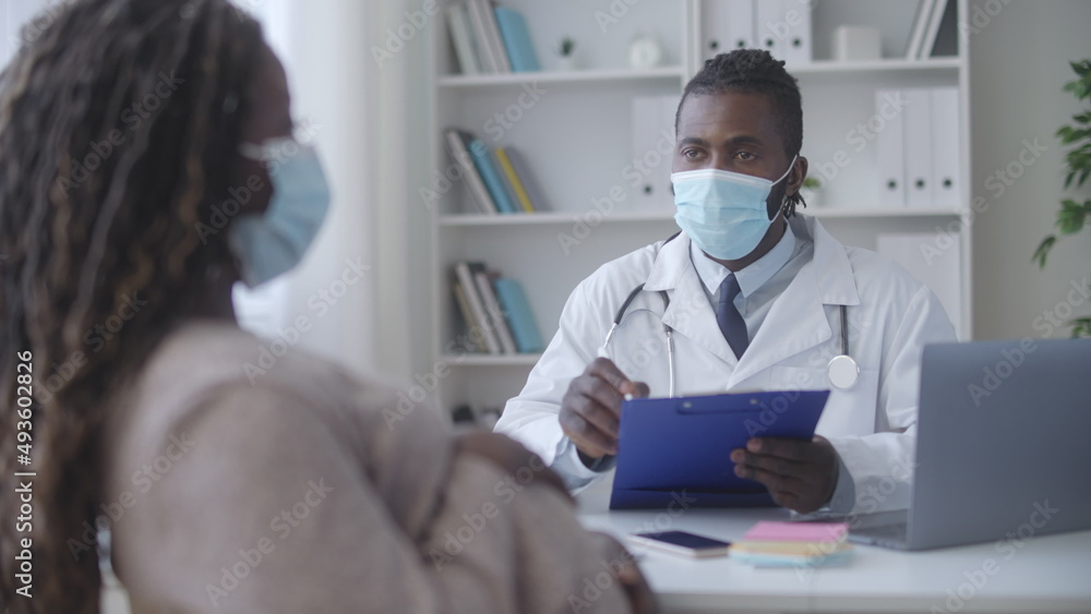 Black pregnant female telling complaints to obstetrician in face mask, check-up Black pregnant female telling complaints to obstetrician in face mask, check-up