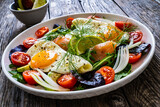 Salmon salad - smoked salmon, sunny side eggs,  avocado and fresh vegetables on wooden table
