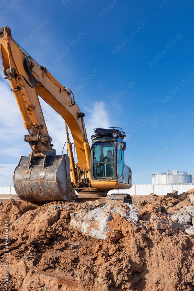 A powerful caterpillar excavator digs the ground against the blue sky. Earthworks with heavy equipment at the construction site. A powerful caterpillar excavator digs the ground against the blue sky. Earthworks with heavy equipment at the construction site.