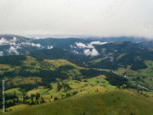 Green slopes of Ukrainian Carpathian mountains in summer. Cloudy morning, low clouds. Aerial drone view.