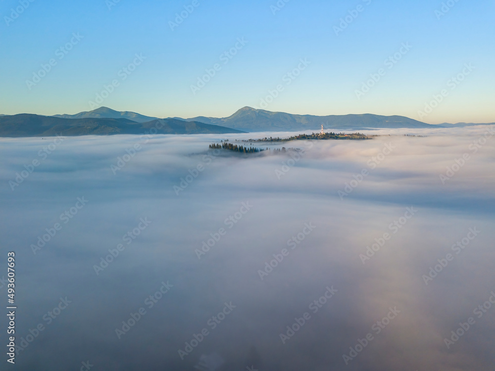 Sunny morning in the foggy Carpathians. A thick layer of fog covers the mountains. Aerial drone view.