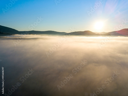 Sunny morning in the foggy Carpathians. A thick layer of fog covers the mountains. Aerial drone view. © Sergey