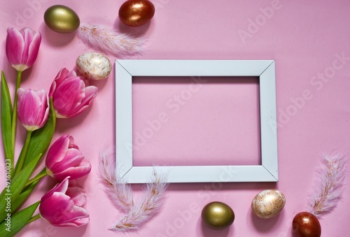Easter composition with blank photo frame, feathers eggs and pink  tulips on pink background. Easter greeting card. Banner
